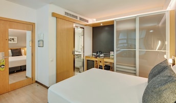 Quarto de hotel com cama, escrivaninha, cadeira, espelho e guarda-roupa.