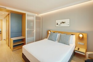 Quarto de hotel com cama, mesa de cabeceira, luminária na parede, porta e quadro pendurado na parede.
