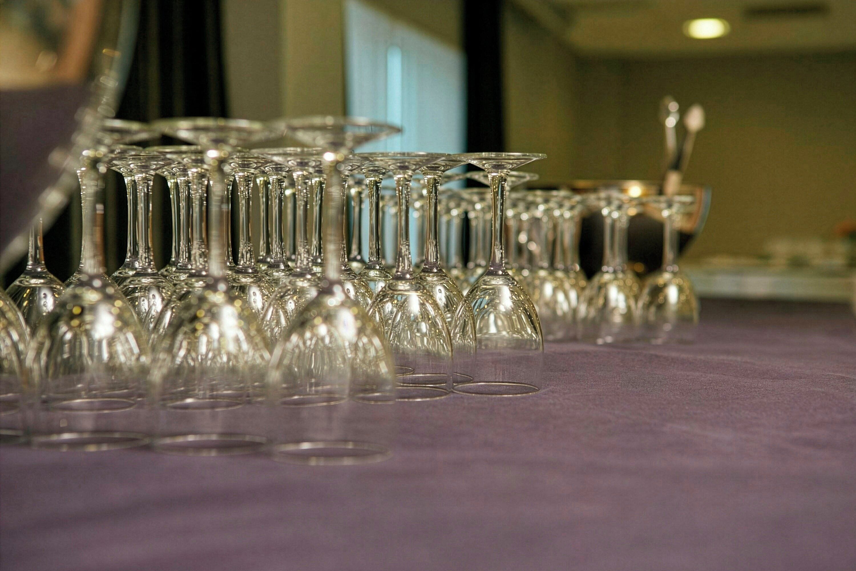 A table with multiple clear glass wine glasses arranged in rows.