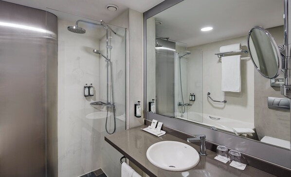 A modern bathroom with a large mirror, a bathtub, a shower with a handheld showerhead, and a sink with a faucet. - Sercotel Caspe (Barcelona)