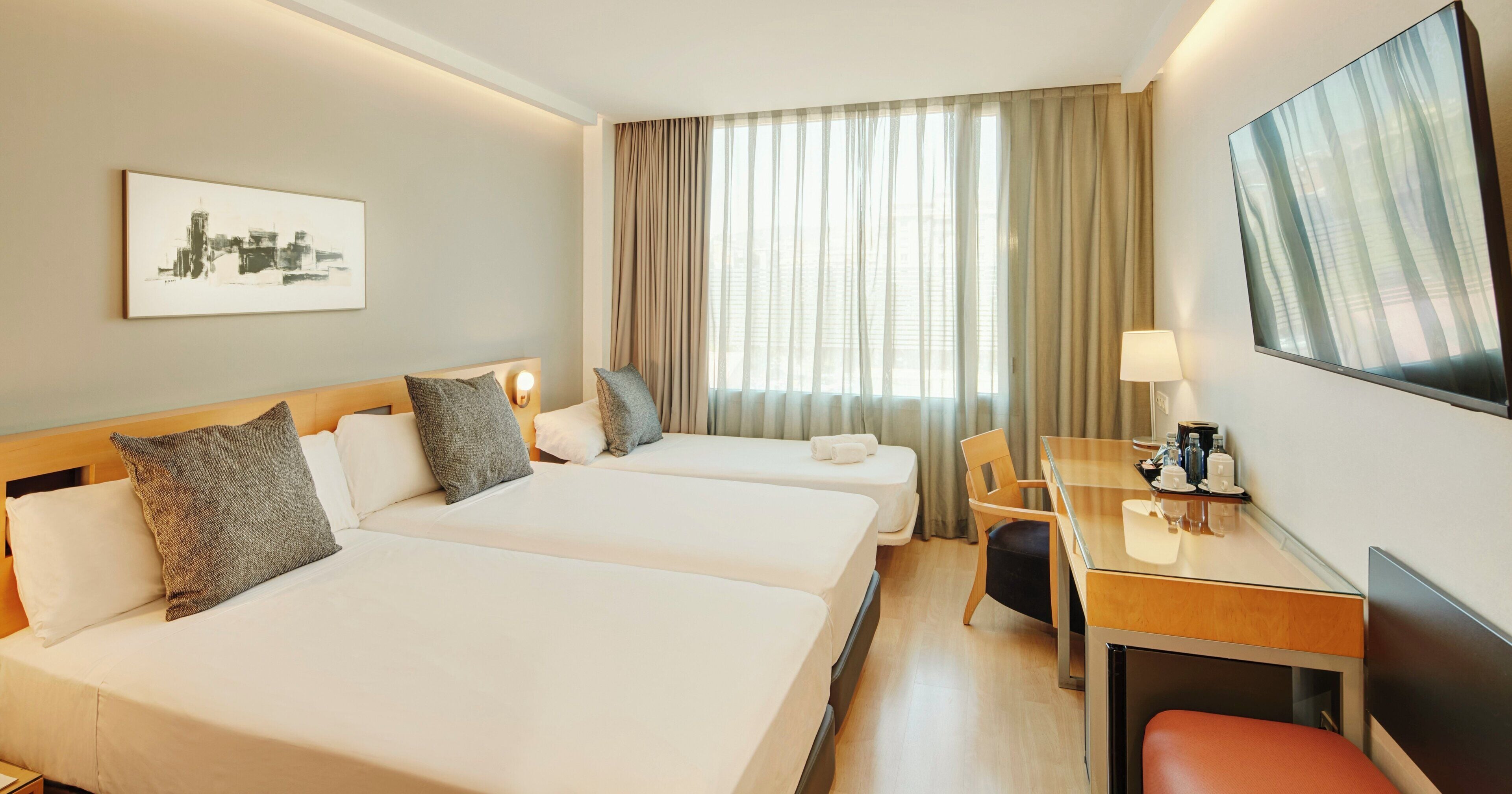 Une chambre d’hôtel avec deux lits, un bureau, une chaise, une lampe et un tableau au mur.