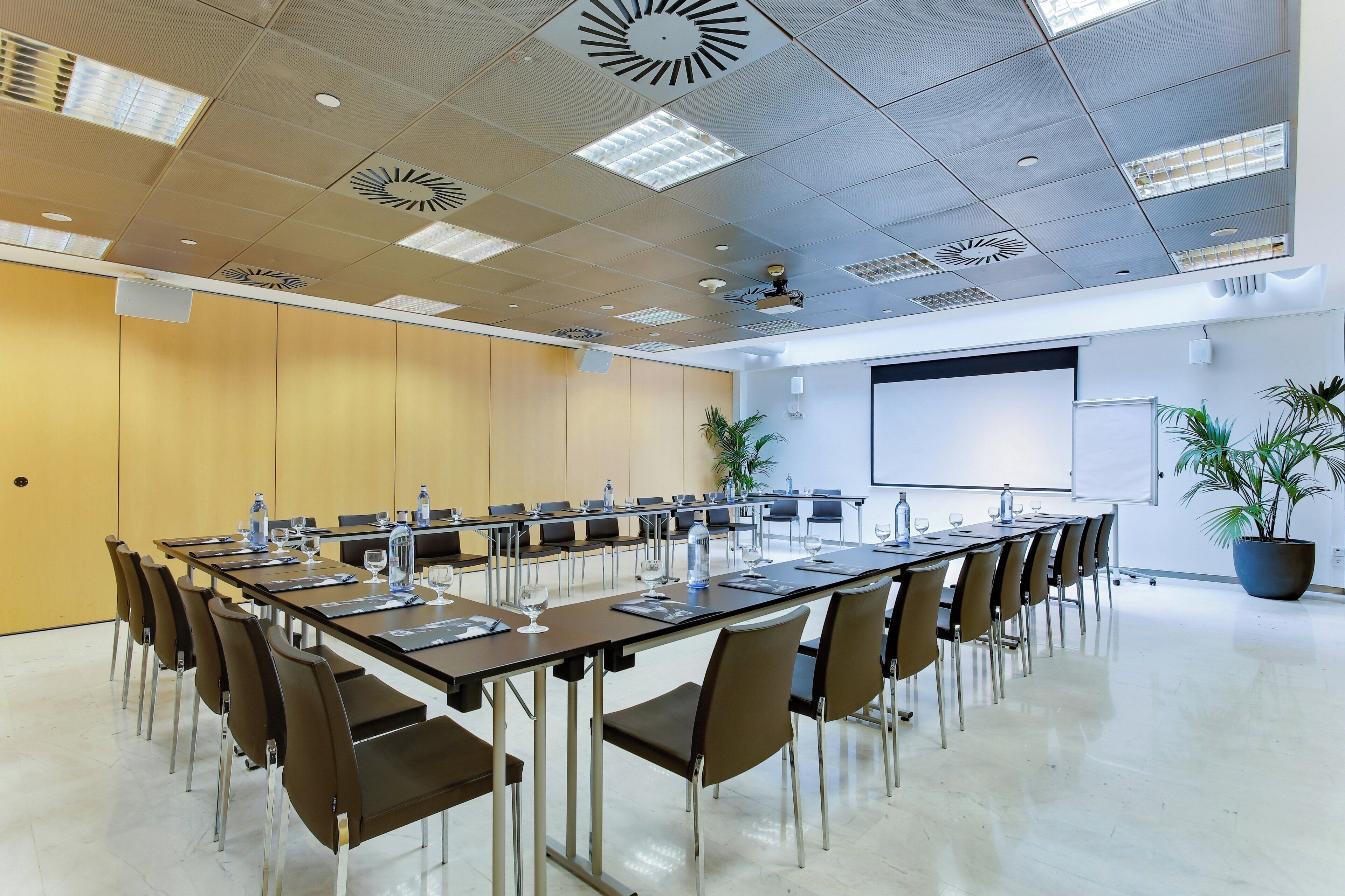 A conference room with a long table, chairs, a projector screen, and a whiteboard.