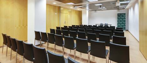 A conference room with rows of black chairs, wooden walls, and ceiling lights.