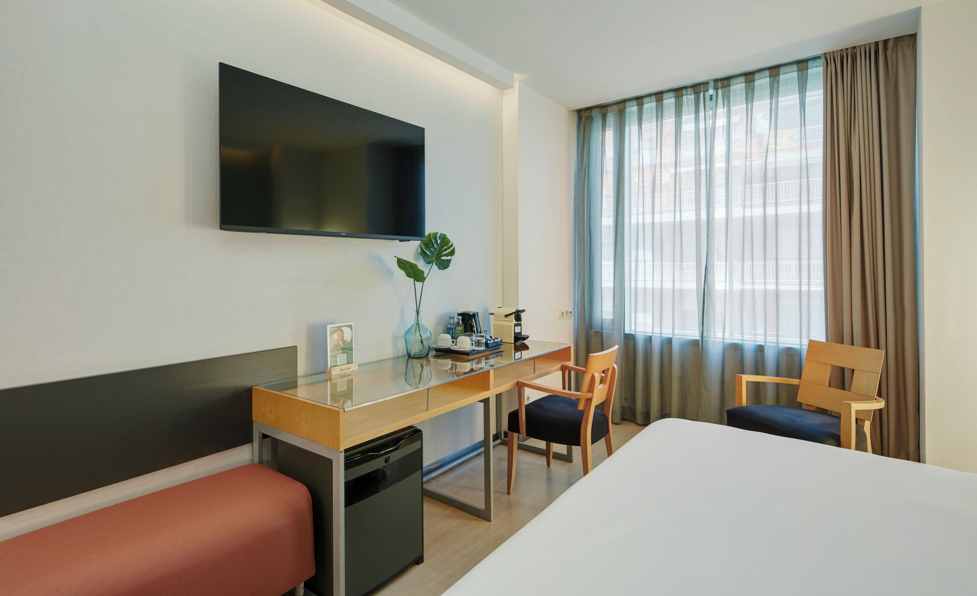 A hotel room with a bed, a desk, a chair, a television, and a window with curtains.