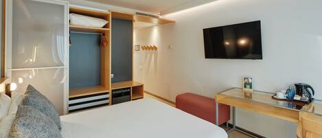 Una habitación de hotel con cama, armario, escritorio, televisor y un pequeño rincón de descanso.