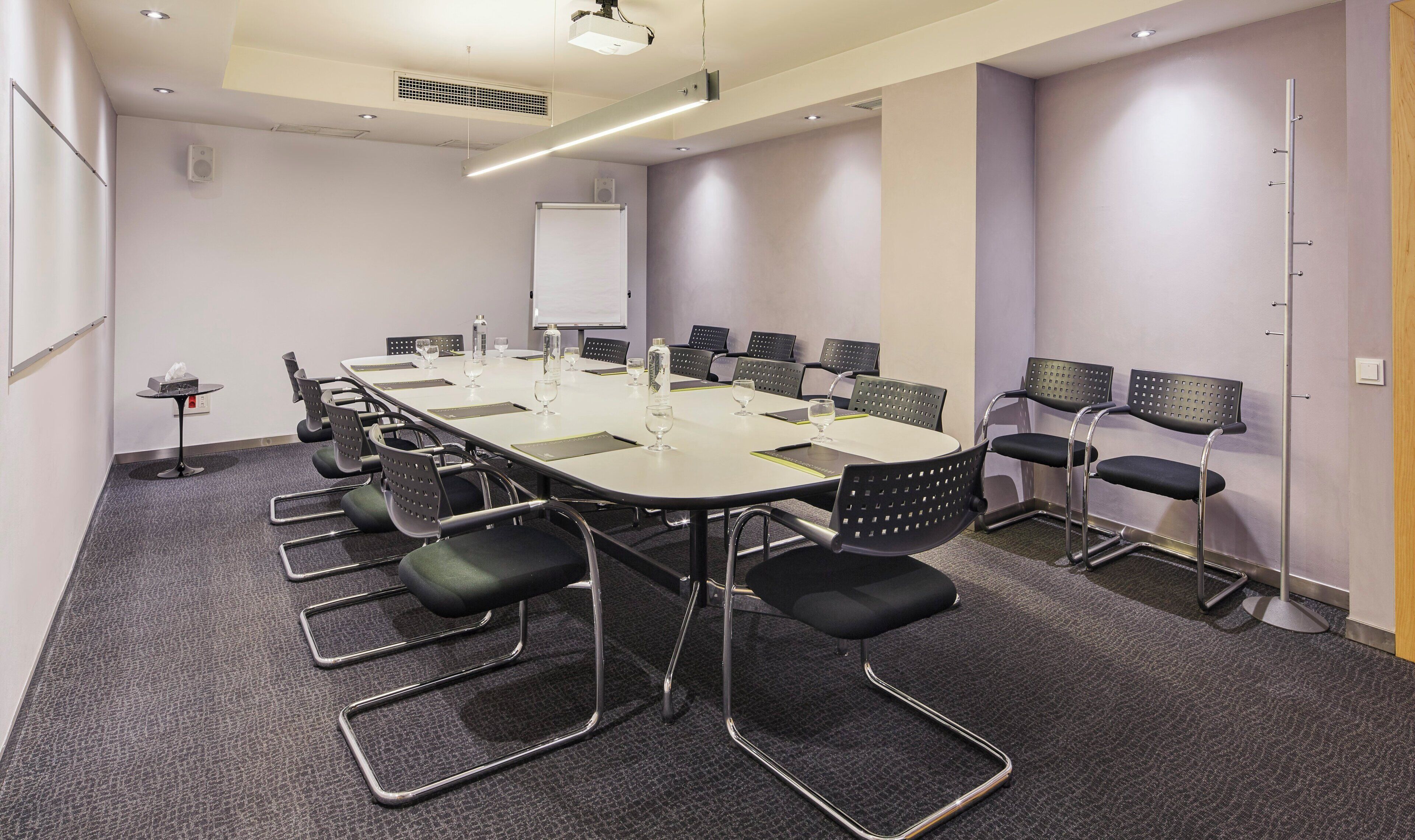 Une salle de conférence équipée d’une longue table, de chaises, d’un tableau blanc et d’un projecteur.