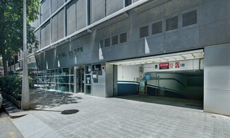 A modern building with a glass facade, a visible entrance, and a sign indicating a parking area.