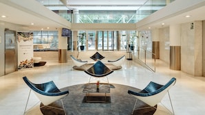 Een ruime lobby met een hoge plafond, modern zitmeubilair en een groot digitaal scherm.