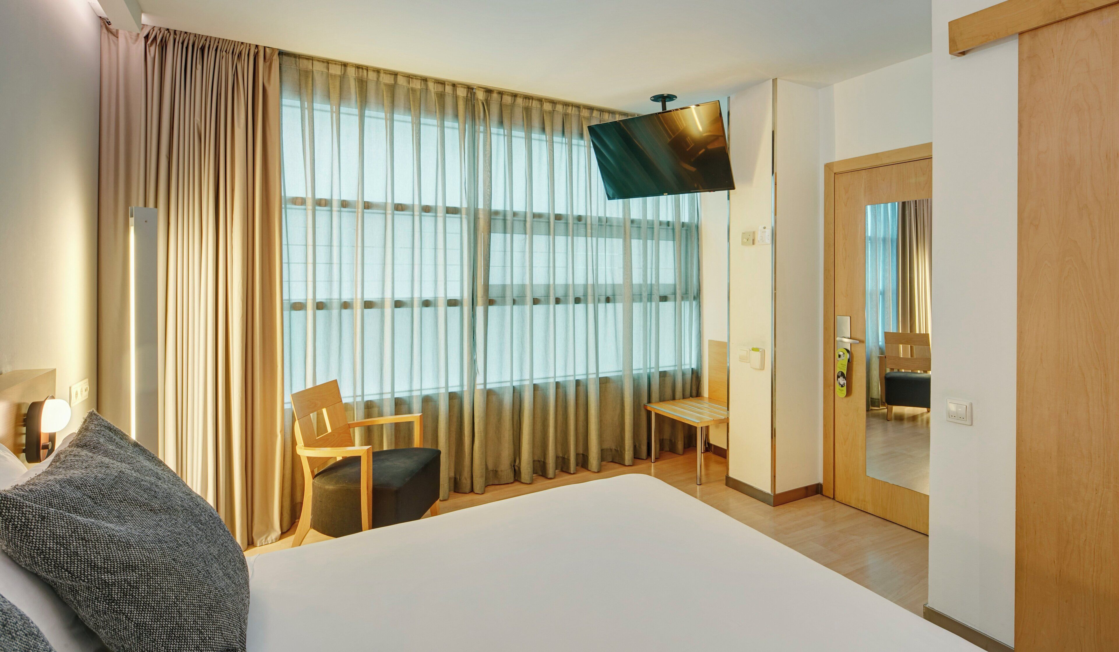 Una habitación de hotel con una cama, dos sillas, un televisor y una puerta.