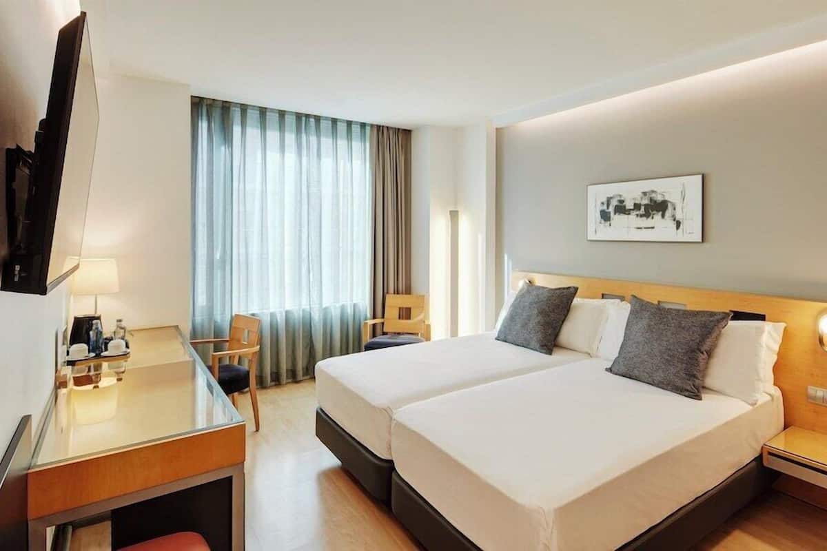 Une chambre d’hôtel avec deux lits, un bureau, une chaise, une télévision et une table de chevet avec une lampe.