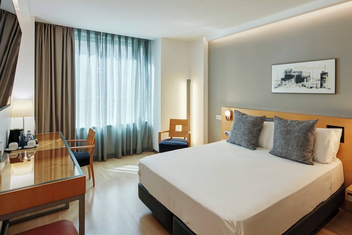 Une chambre d’hôtel avec un lit, des tables de chevet, un bureau, une chaise, une lampe et un tableau au mur.