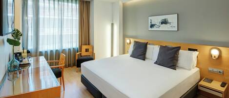 A hotel room with a bed, bedside table, desk, chair, and a large window with curtains.