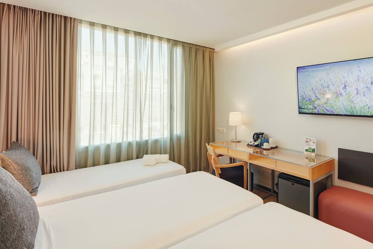 Une chambre d’hôtel avec deux lits, un bureau avec une lampe, une télévision et un petit réfrigérateur.