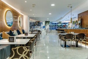 A modern restaurant with a long counter, seating area with patterned chairs, and a mural on the wall.