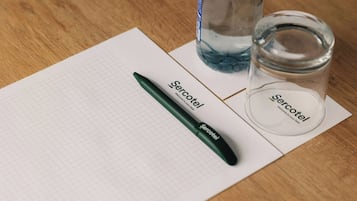 Carta millimetrata, una penna, una bottiglia di vetro e un vasetto su un piano di legno.