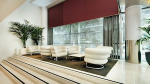 Een moderne lobby met een trap, witte fauteuils en grote ramen.