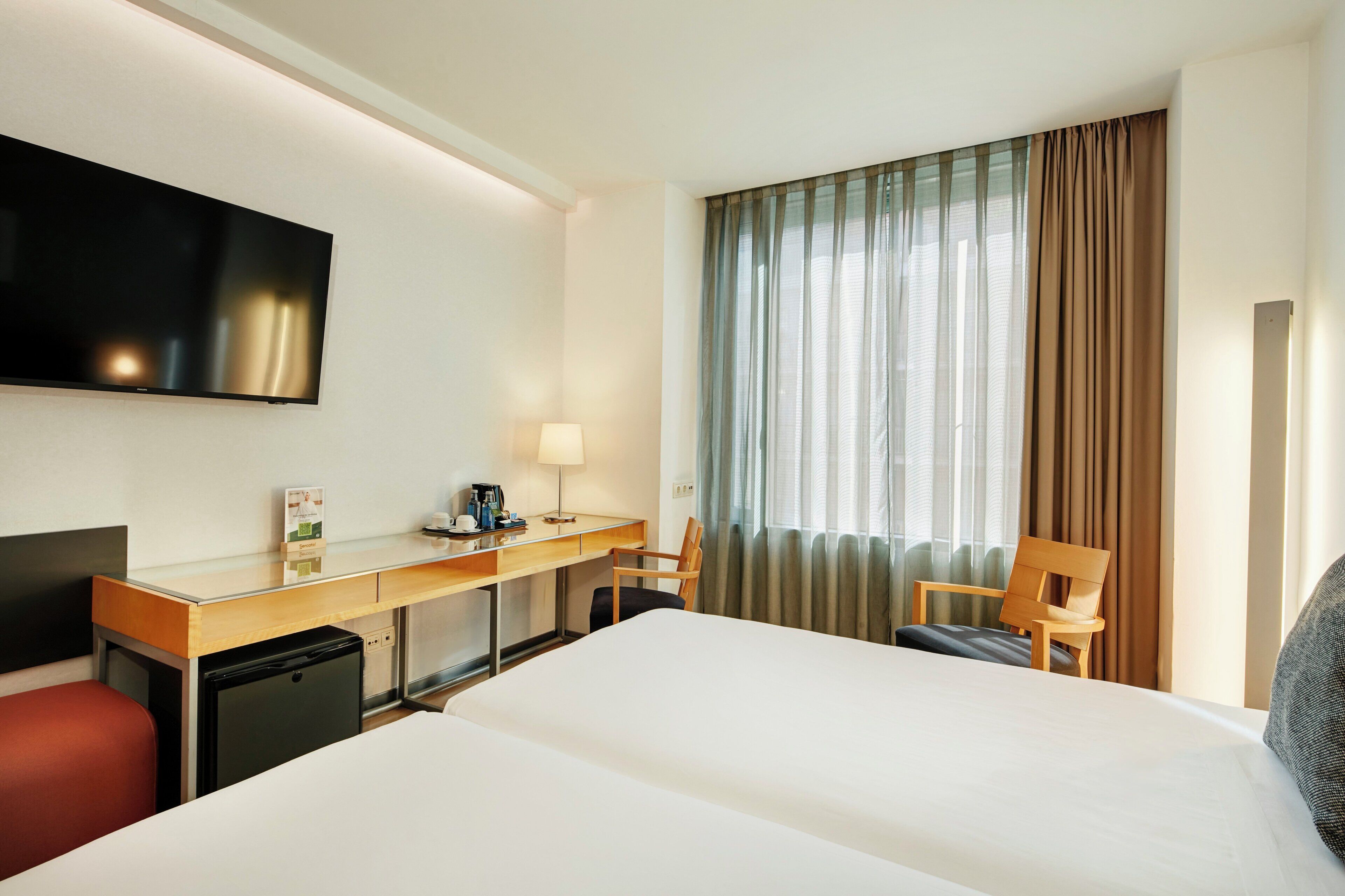 Una habitación de hotel con cama, escritorio, silla, televisor y cortinas.