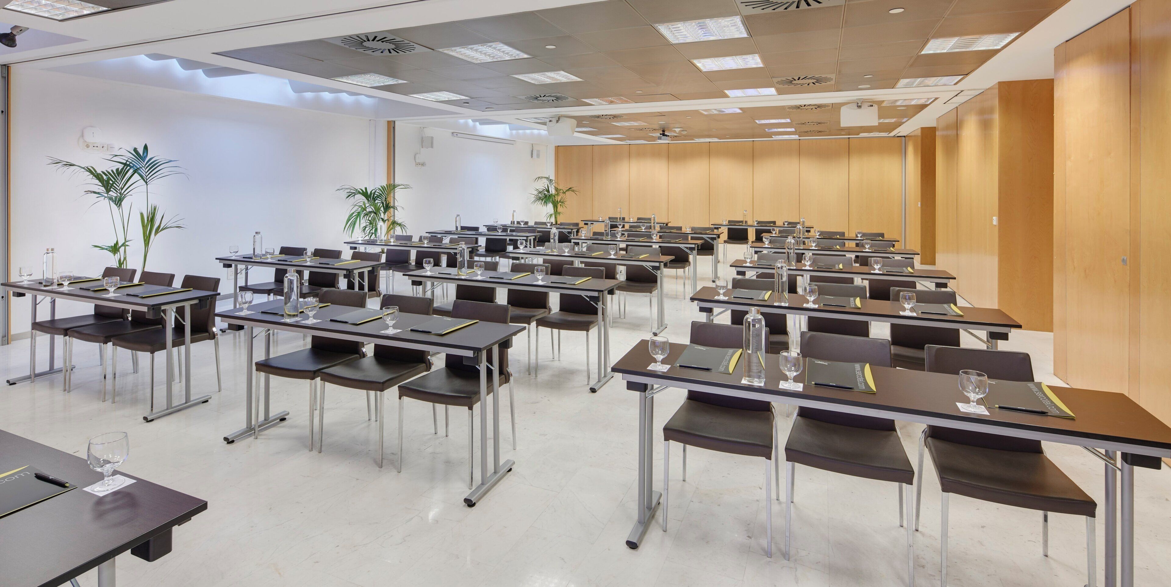 A conference room with rows of tables, chairs, and potted plants.