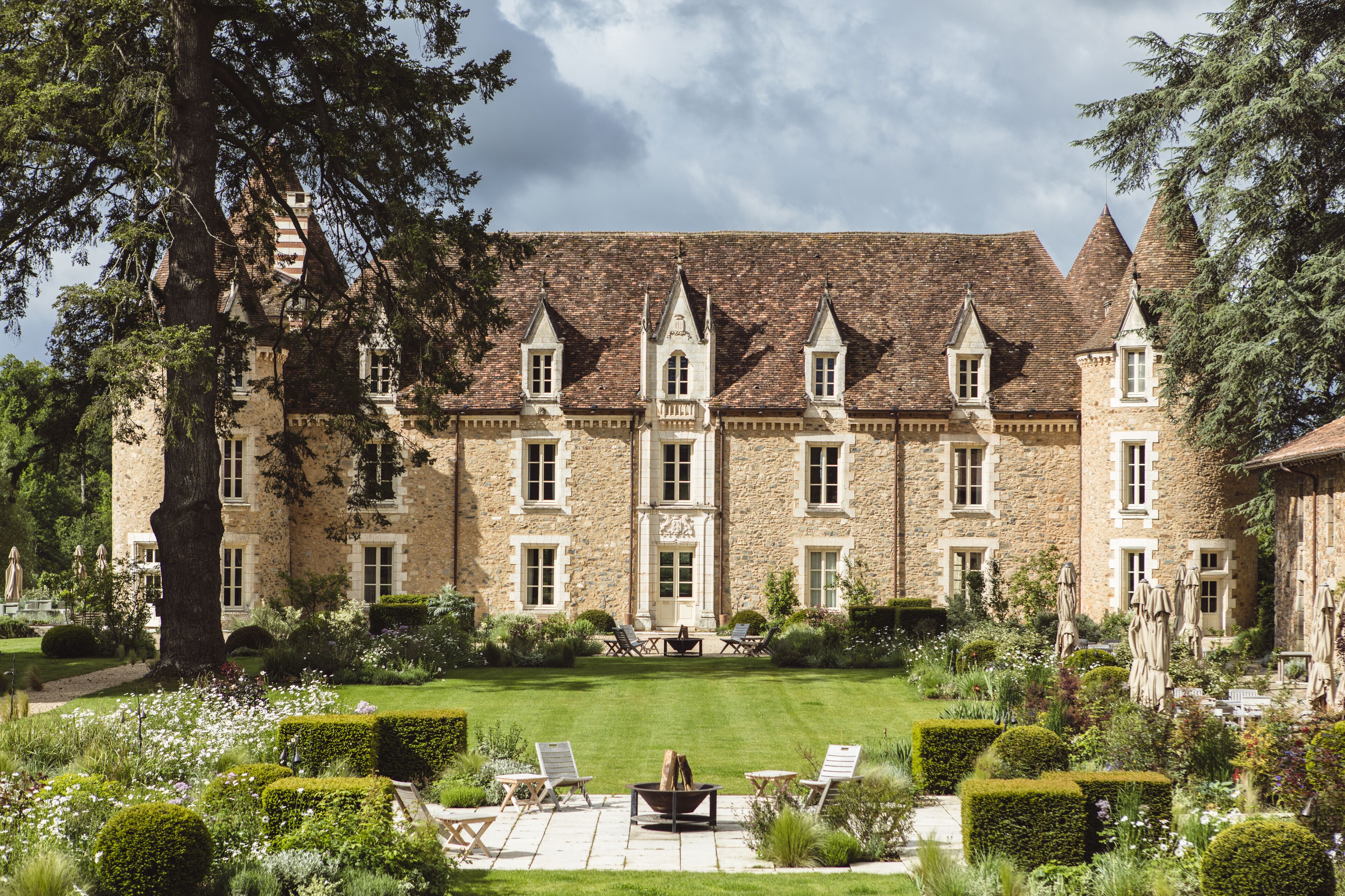 A large stone building with multiple towers and a well-maintained garden with seating areas.