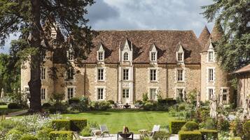 A large stone building with multiple towers and a well-maintained garden with seating areas.