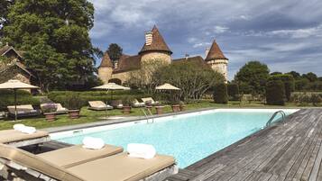 A swimming pool with lounge chairs and umbrellas, surrounded by a castle-like building with multiple towers.