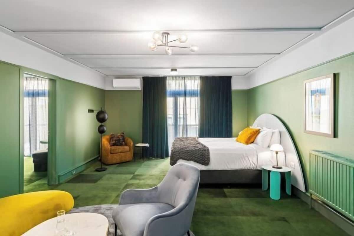 A room with a bed, a chair, a small table, a floor lamp, and a radiator.