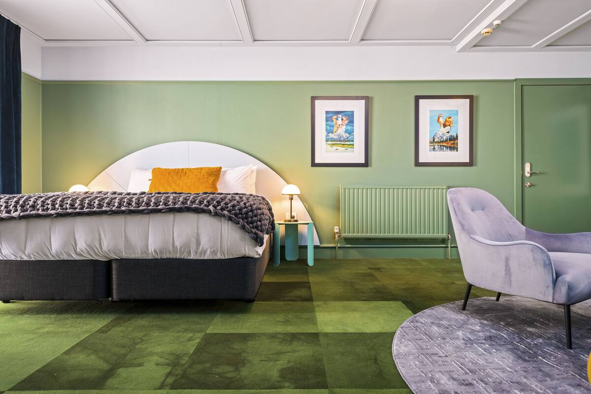 A bedroom with a bed, a chair, a nightstand, and two framed pictures on the wall.