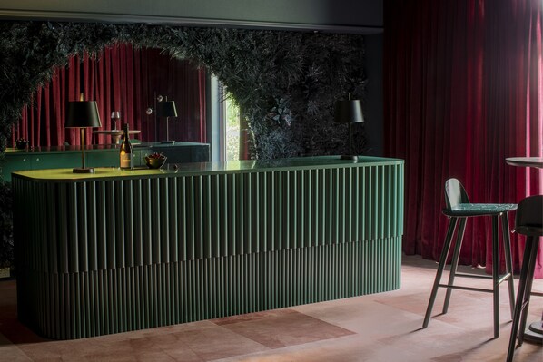 Un área de bar moderna con una barra verde, dos taburetes negros y una pared decorativa con follaje.