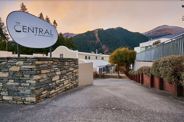 Entrada de un hotel con un muro de piedra, un cartel que dice "The Central by Nami Hotels" y montañas al fondo.
