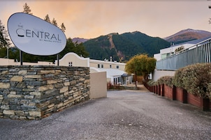 A hotel entrance with a stone wall, a sign reading "The Central by Nami Hotels," and a mountain backdrop.