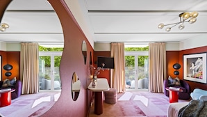 A modern hotel room with a large window, a round mirror, a round table, a sofa, and a bed.