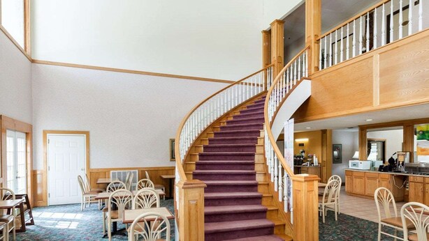 A spacious hotel lobby with a curved wooden staircase, multiple seating areas, and a reception desk.