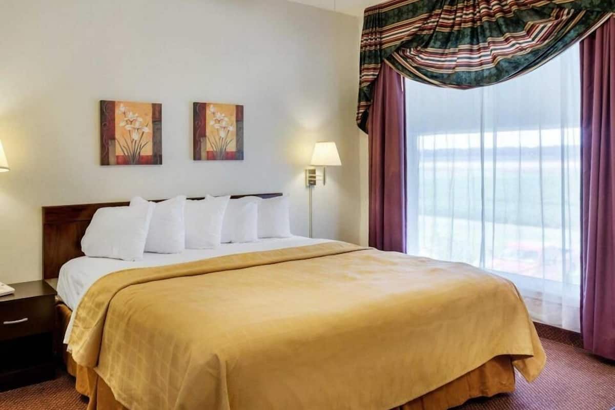 A hotel room with a large bed, two wall-mounted lamps, and a window with curtains.