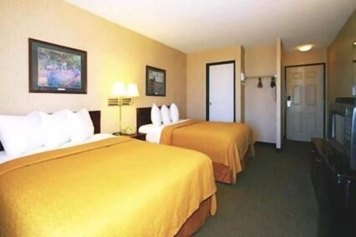 A hotel room with two beds, a television, a door, and a painting on the wall.