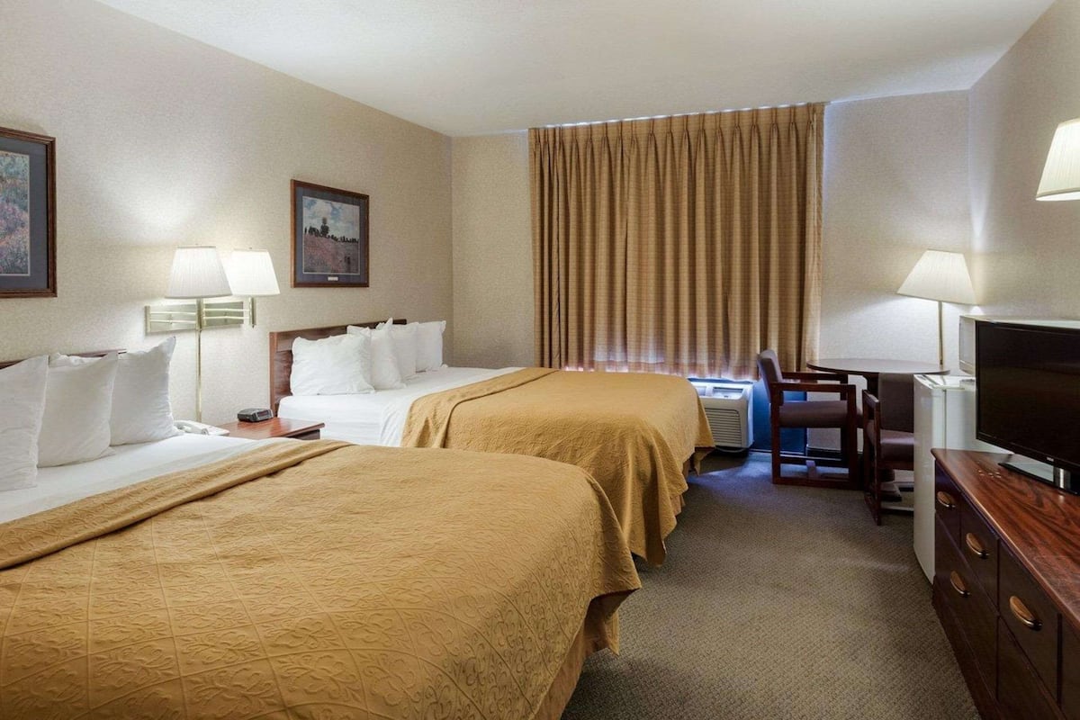 A hotel room with two beds, a desk, a television, and a window with curtains.