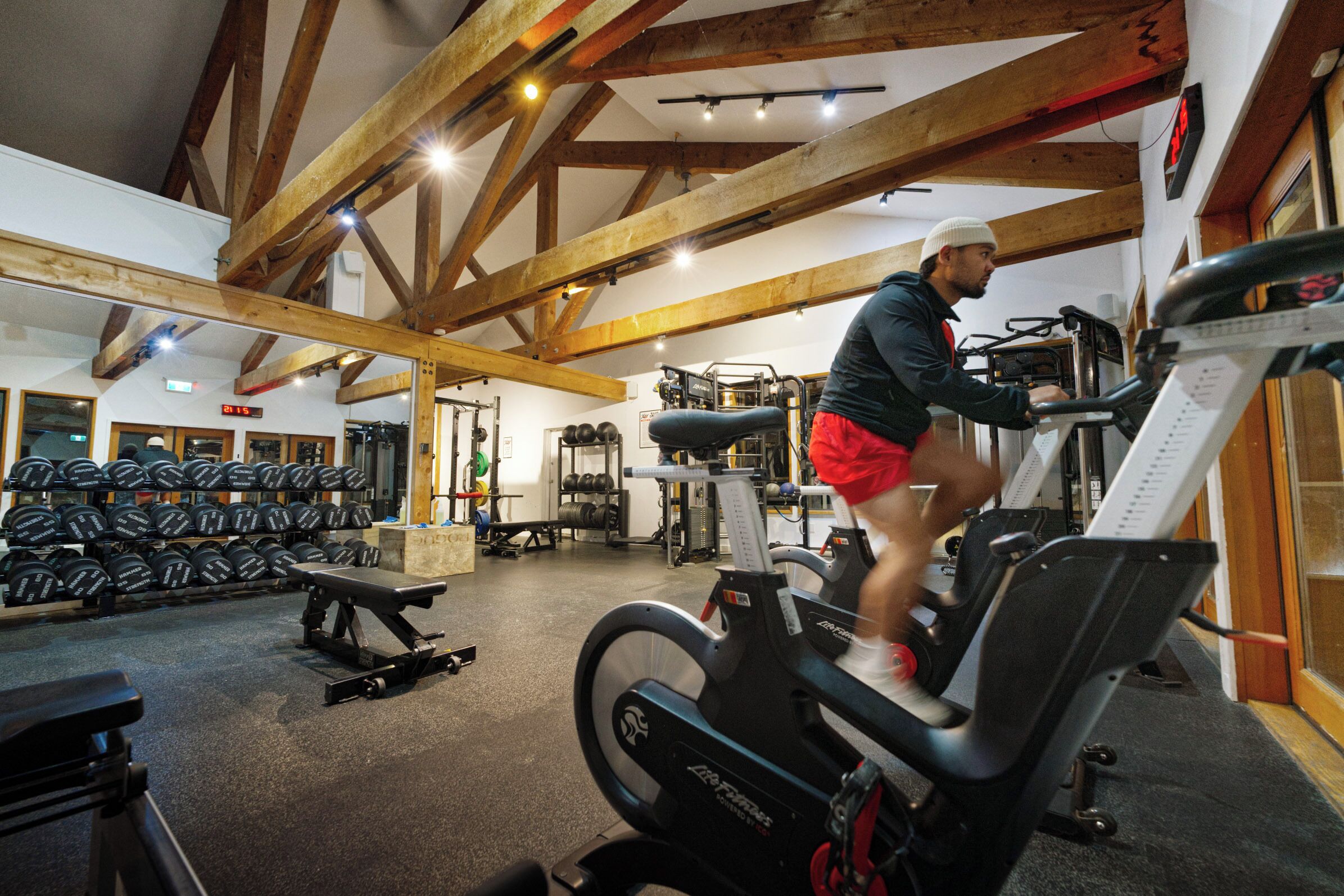 A gym with exercise equipment, weight racks, and a wooden ceiling structure.