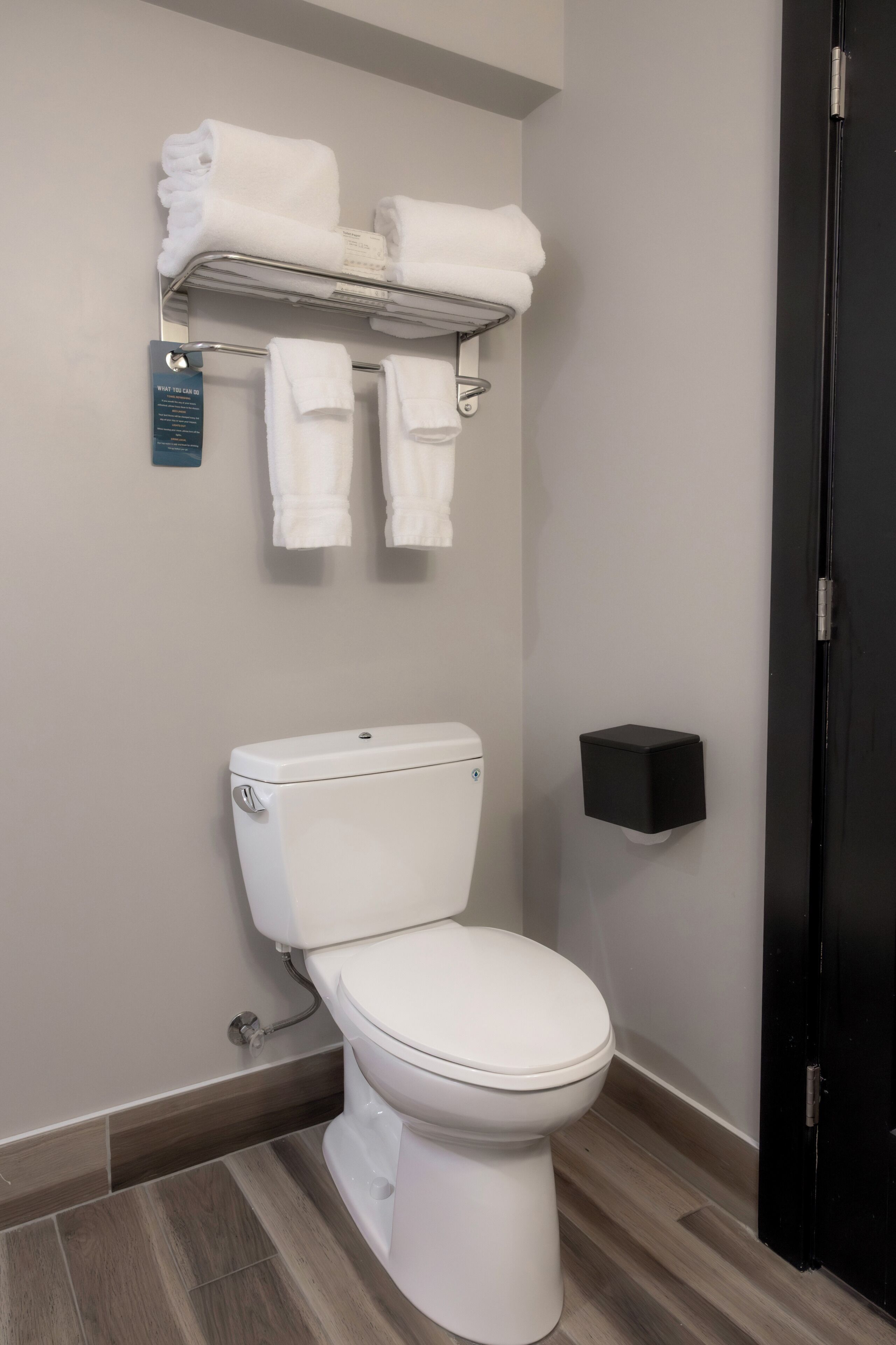 A modern bathroom with a toilet, a towel rack with folded towels, and a black wall-mounted object.