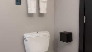 A modern bathroom with a toilet, a towel rack with folded towels, and a black wall-mounted object.