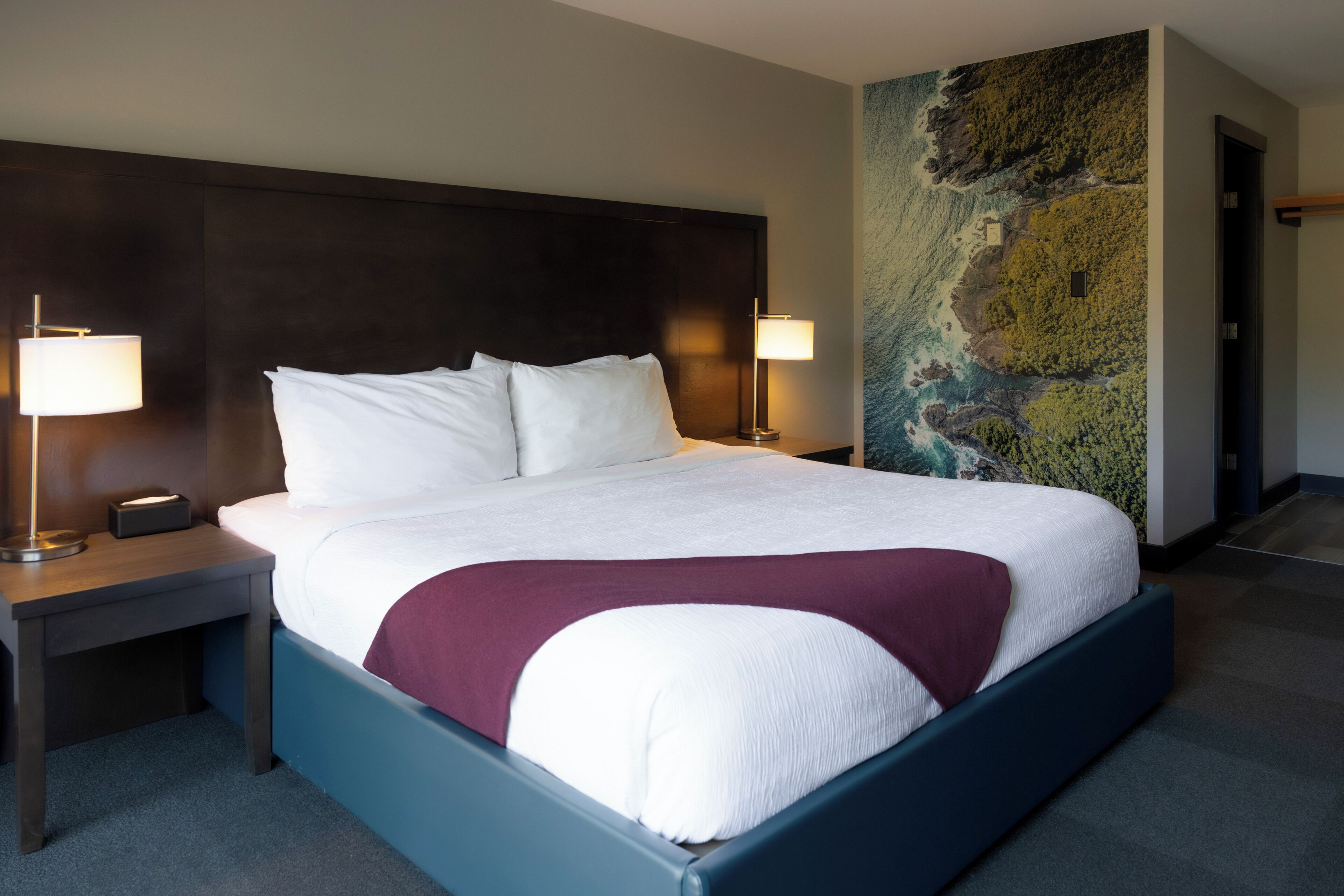 A hotel room with a large bed, two bedside lamps, a nightstand, and a wall mural.