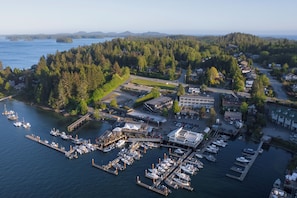 An aerial view of a marina with boats docked, a small town with houses and buildings, and a forested hill in the background. - Tofino Resort & Marina (Tofino)