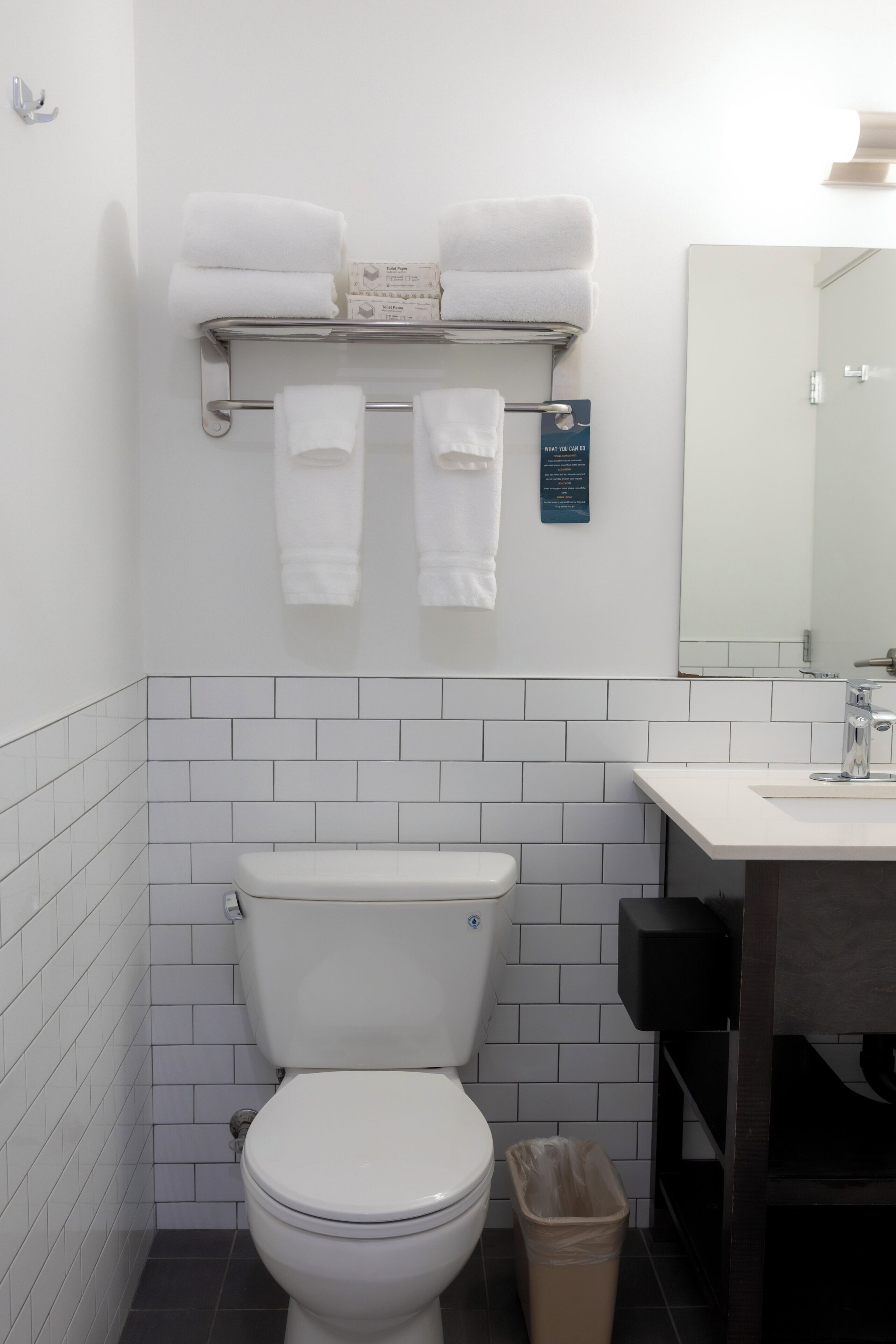 Une salle de bain avec des toilettes blanches, un lavabo et un miroir. Des serviettes sont posées sur un porte-serviettes au-dessus des toilettes.