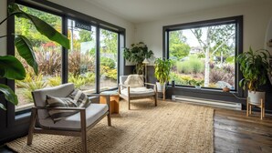 Una sala de estar moderna con ventanas amplias, un sofá, un sillón y plantas en macetas.