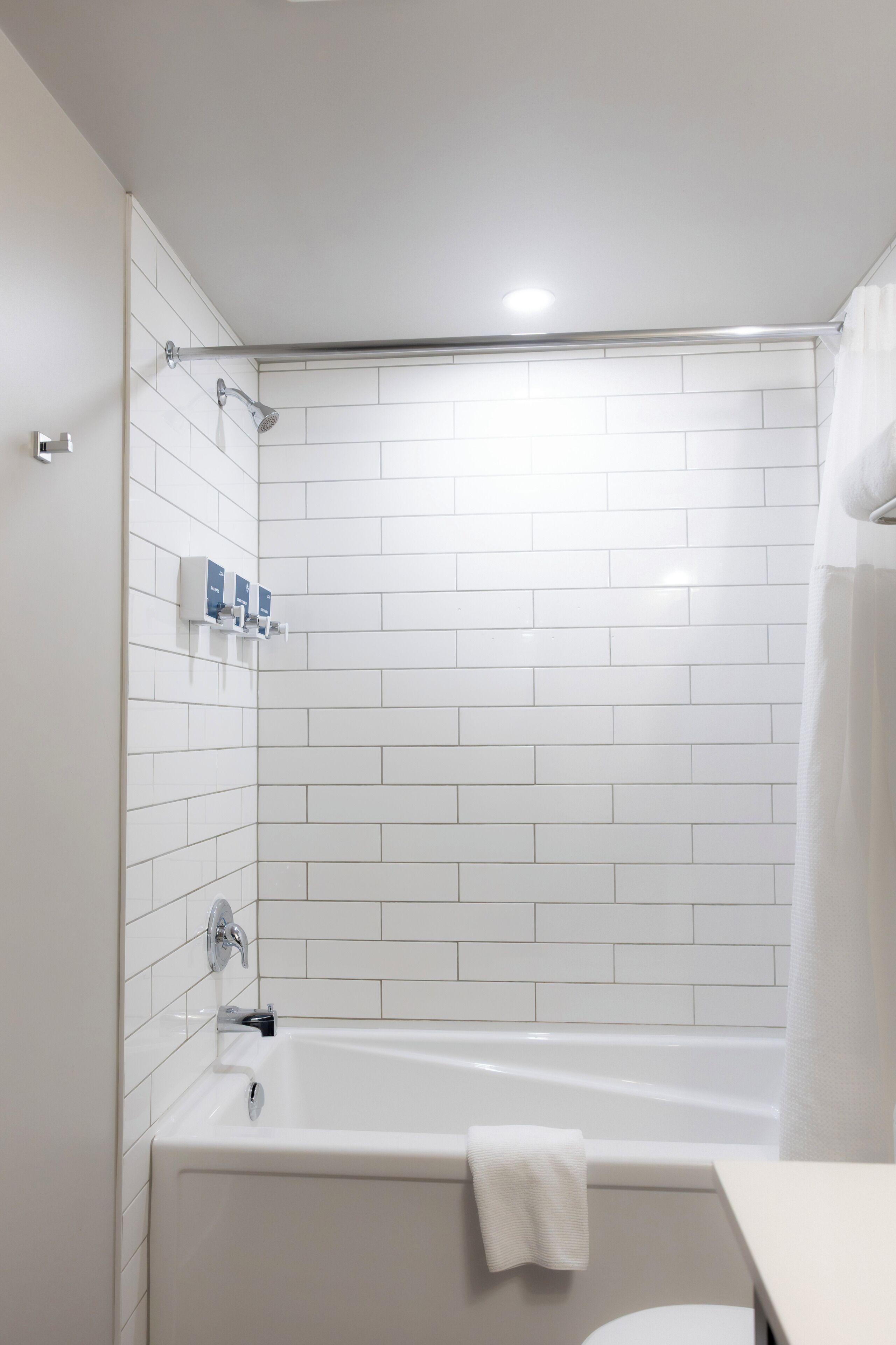Une salle de bain moderne avec des murs recouverts de carreaux blancs, une baignoire, une douche et des toilettes.
