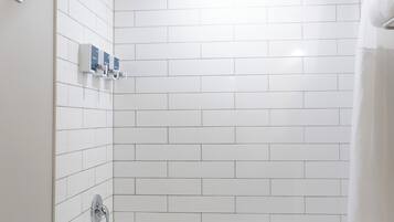 Une salle de bain moderne avec des murs recouverts de carreaux blancs, une baignoire, une douche et des toilettes.