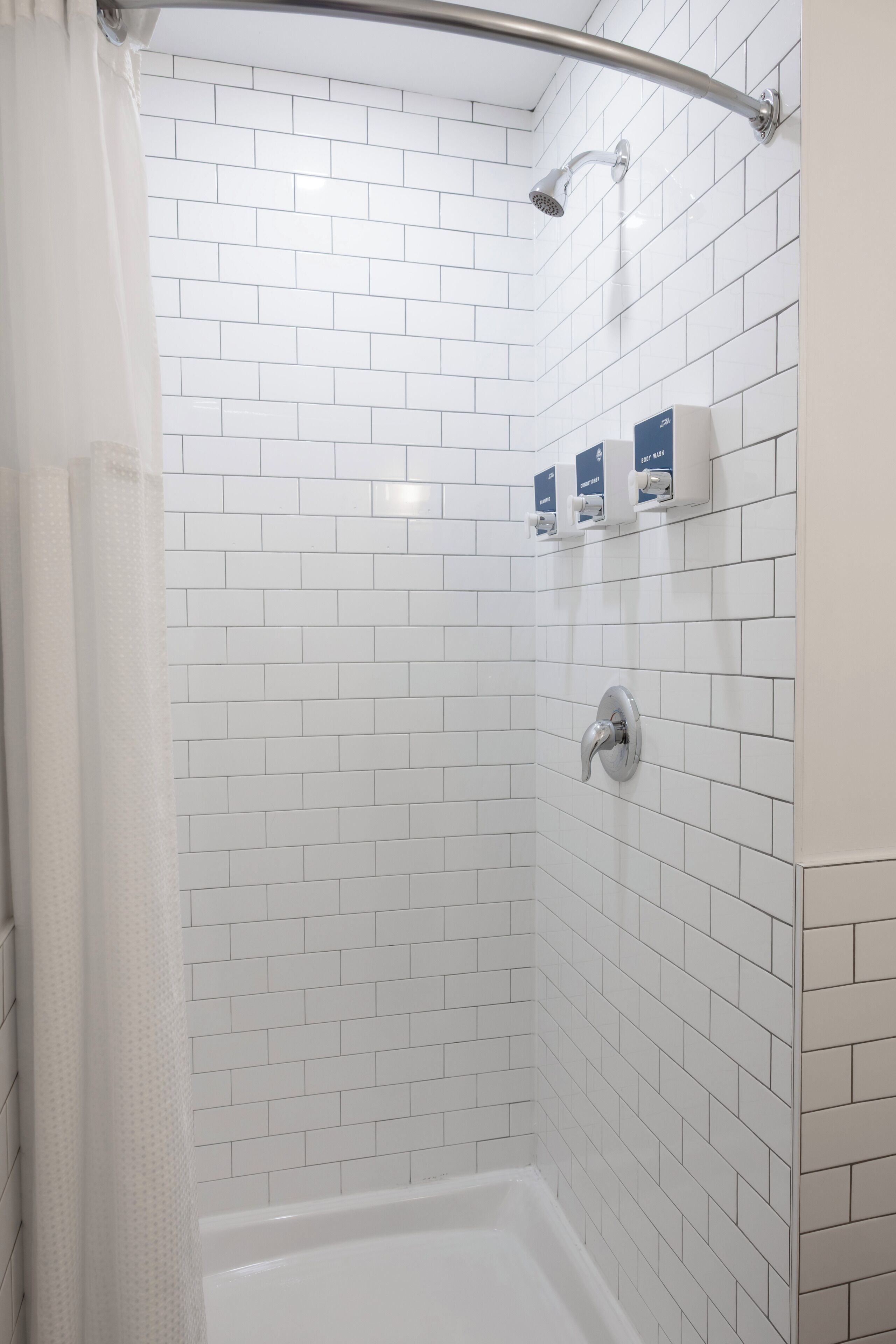 A shower area with white tiled walls, a showerhead, and a hand shower.