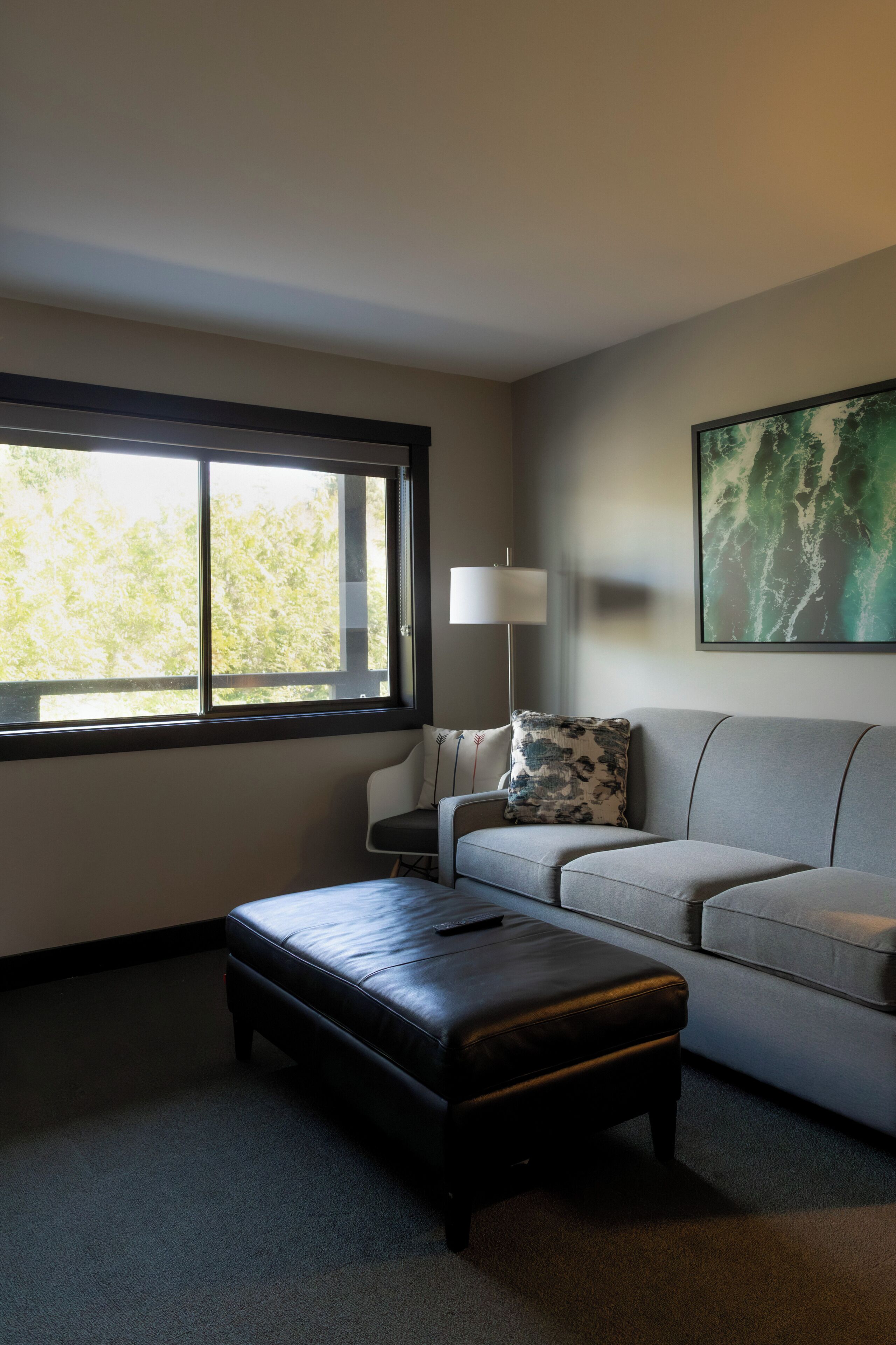 A modern living room with a sofa, a side table, a lamp, a window, and a painting on the wall.