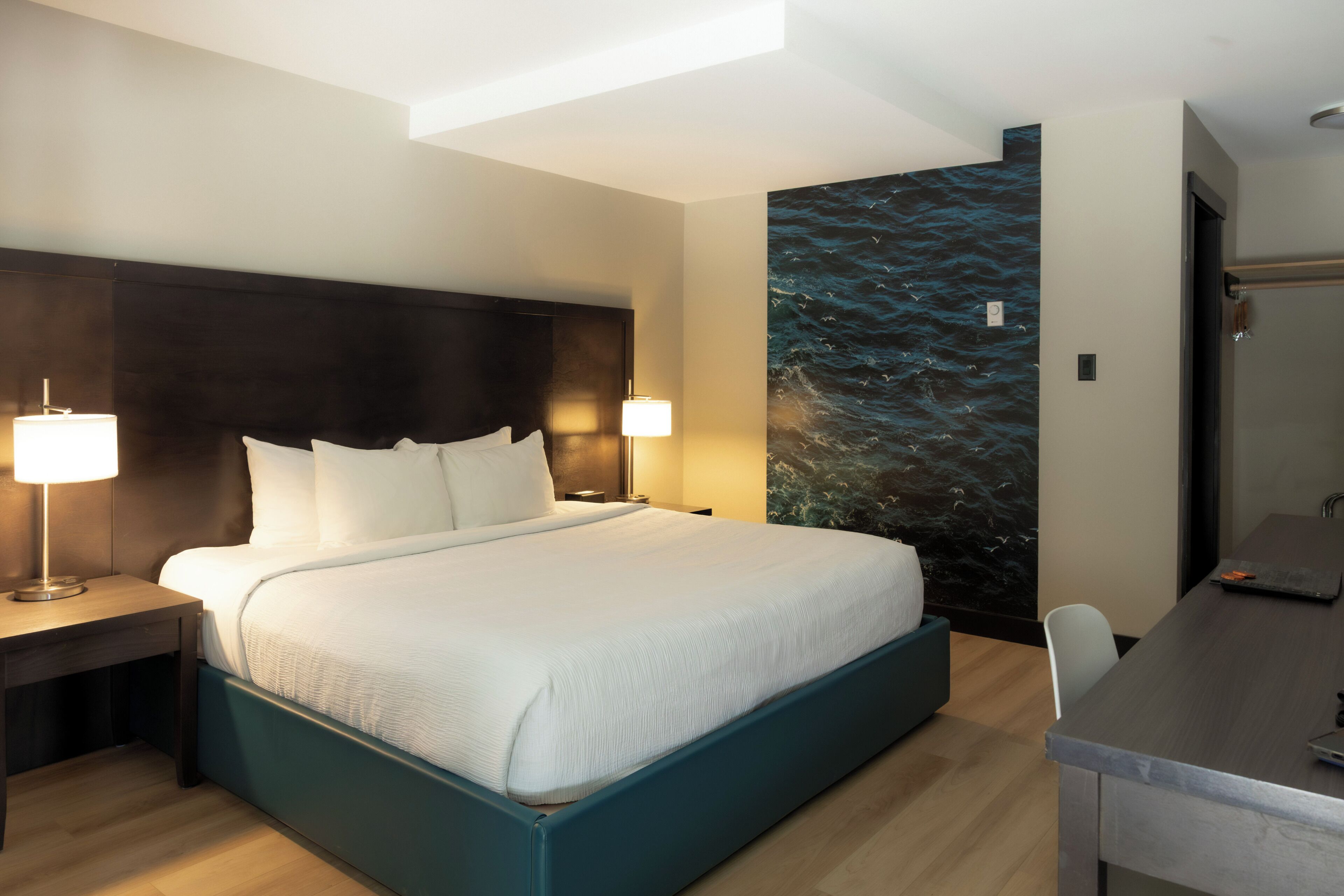 Una habitación de hotel moderna con una cama grande, lámparas de noche, un escritorio y un mural en la pared.