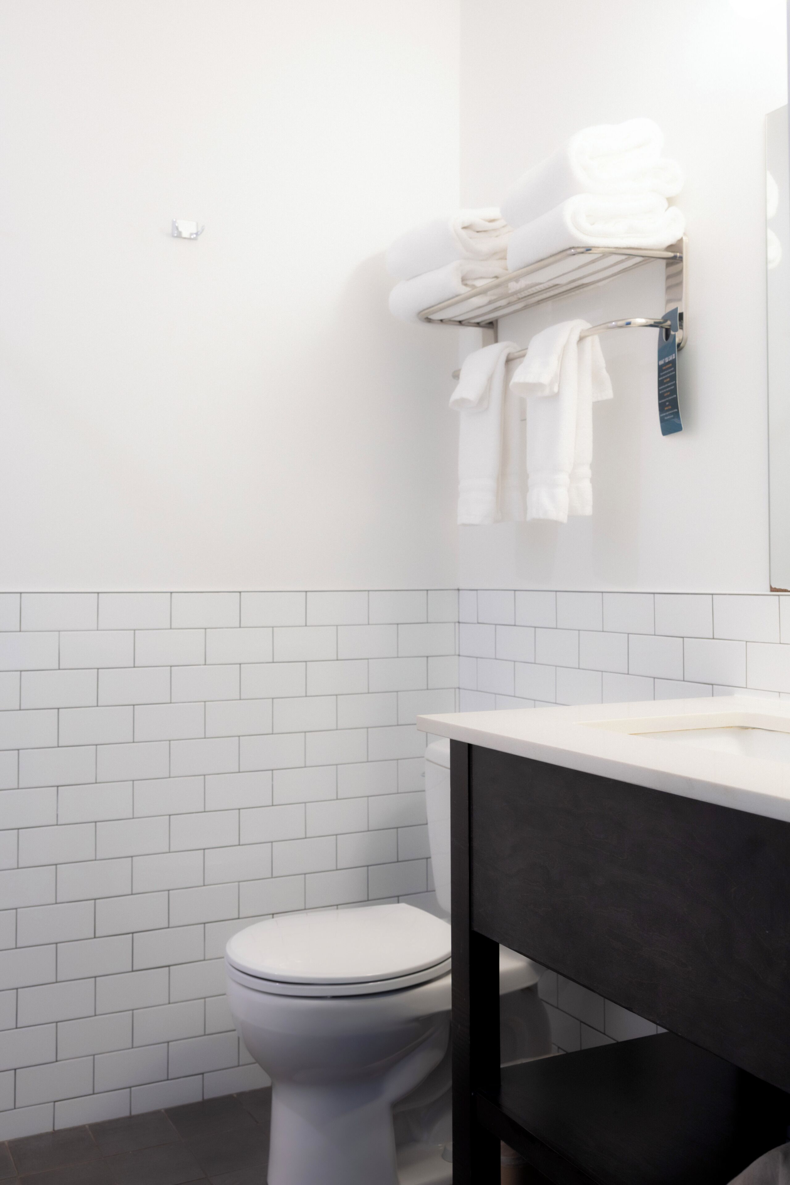 A bathroom with a white toilet, a black vanity, and a towel rack with folded towels.