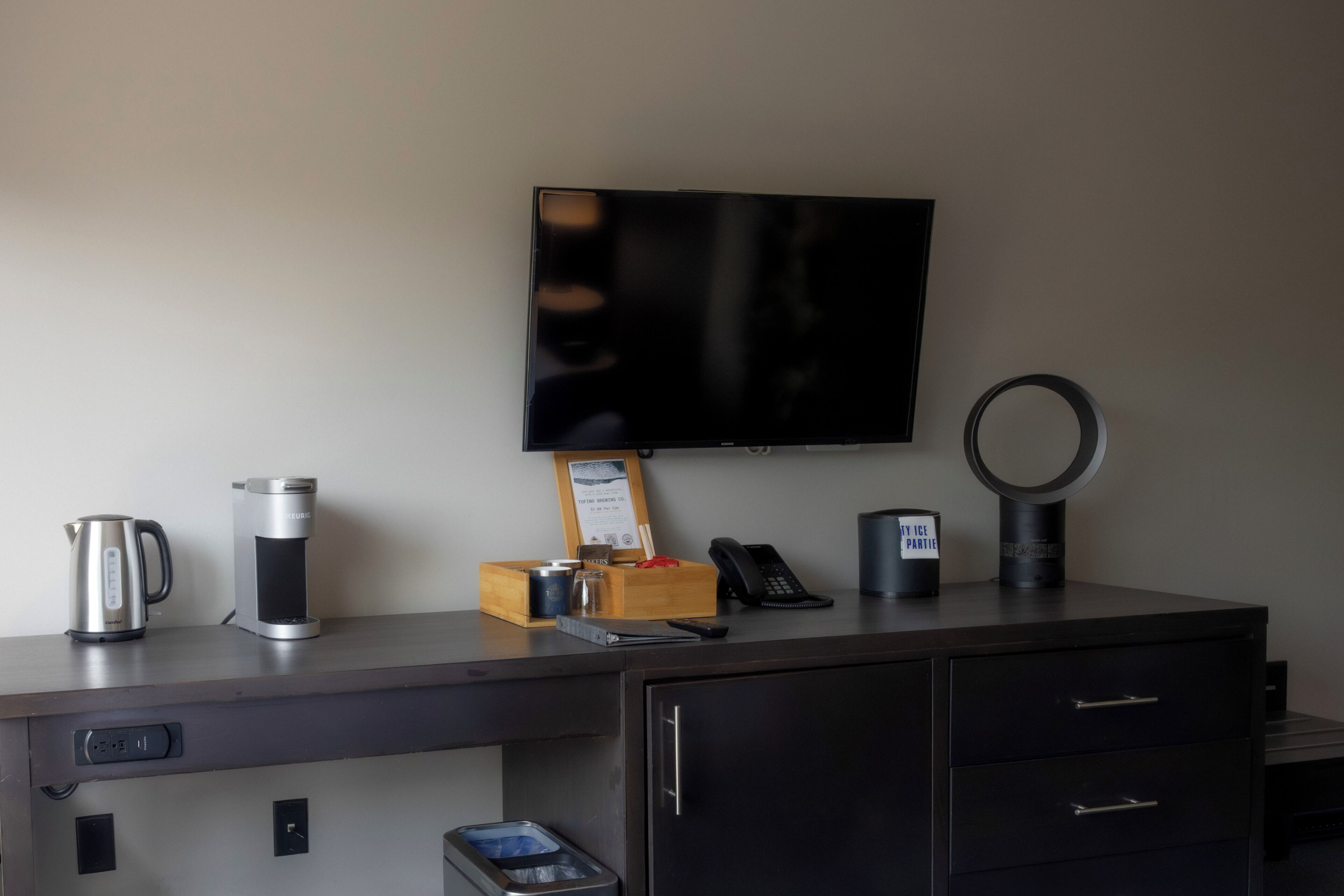 A hotel room with a flat-screen TV, a coffee maker, a phone, and a ring light on the desk.