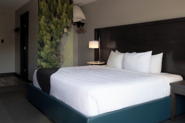 Habitación de hotel con una cama grande, una mesita de noche con lámpara, un muro con jardín vertical verde y un cabecero oscuro.
